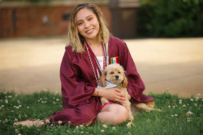 Cinthia Arreola穿着毕业典礼礼服和狗坐在一起