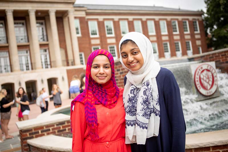 两名戴着彩色头巾的学生在光束喷泉前微笑