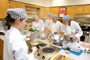 穿着白色厨师长袍的学生在皇冠app营养项目的厨房里准备一顿饭.