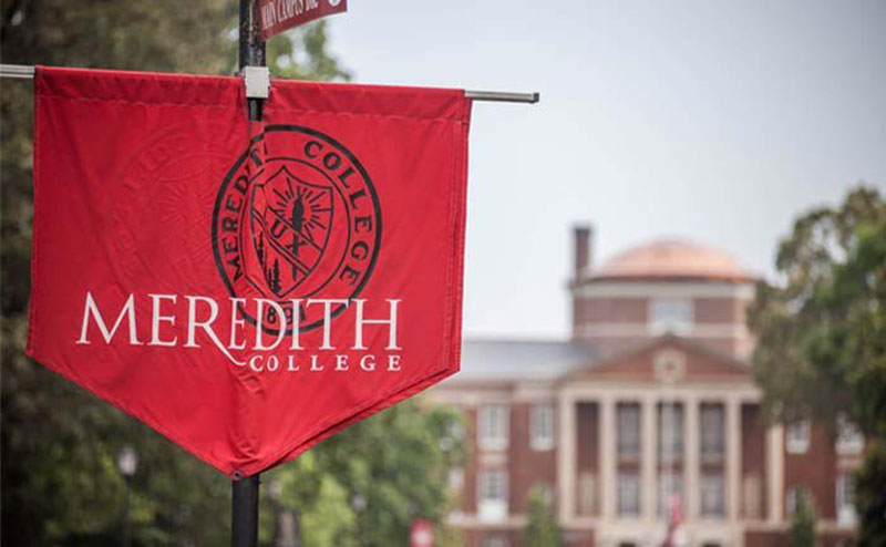 A Meredith College banner in the foreground with Johnson Hall in the background.