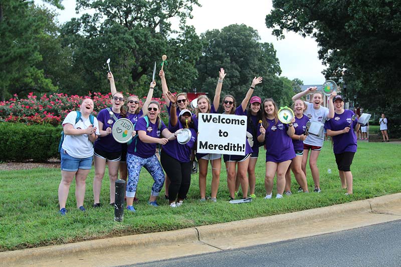 Group of cheering Meredith students at Main Campus Drive with a Welcome to Meredith sign