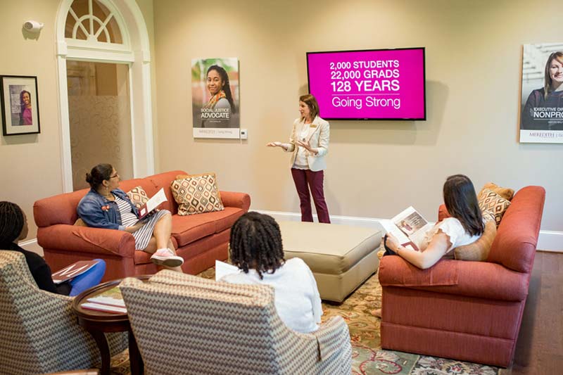 A woman talking to a group of girls on couches.