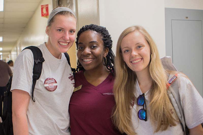 Three students standing together smiling in hallway