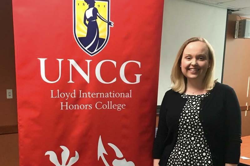 Photo of Catherine Koontz in front of a banner that says UNCG Lloyd International Honors College