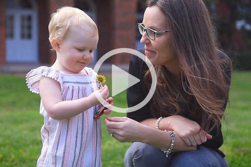 Click on image of mother looking at child holding yellow flower to play video in modal