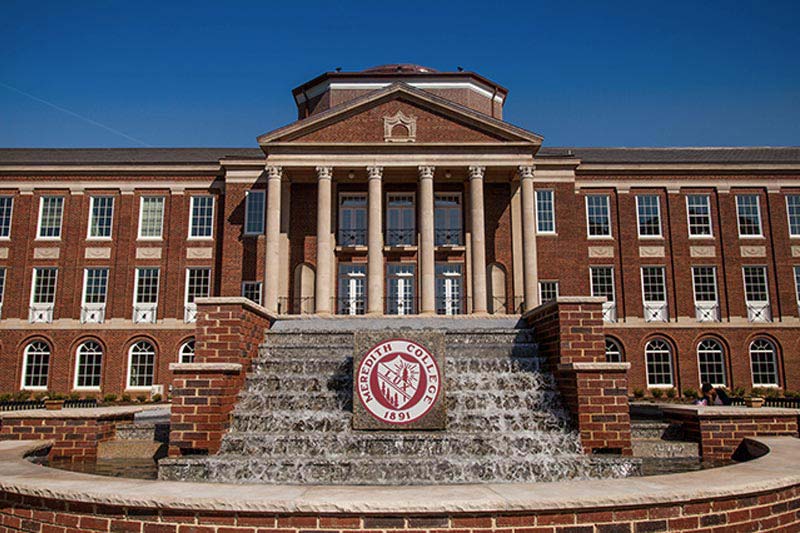 Johnson Hall with fountain in front. The fountain has tiers that look like steps, and features the Meredith College seal