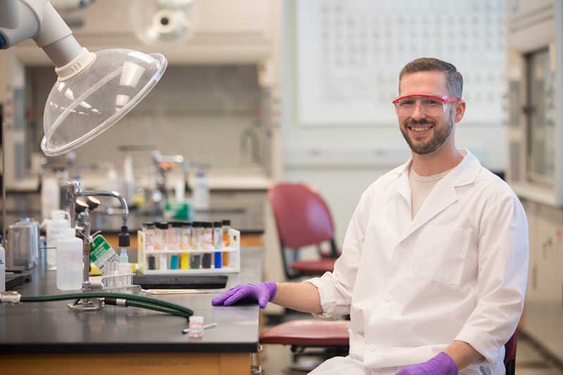 Hunter Peden in a white lab coat sitting in a Biology lab