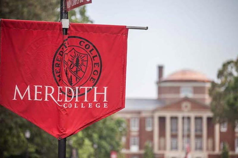 Meredith College banner with Johnson Hall in the background. The banner is maroon with the Meredith seal in black, and the words Meredith College in white