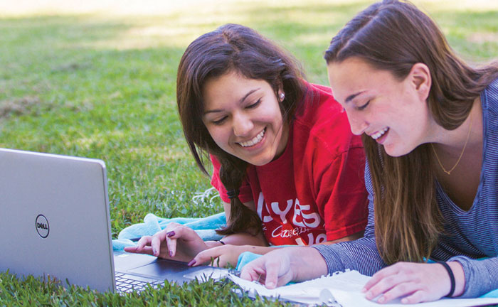 Two students outside on blanket reviewing notes and looking at computer.