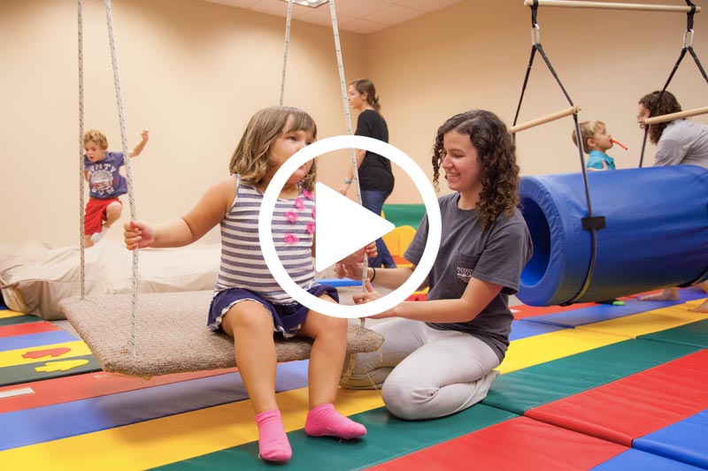 Click on image of Students working with autistic children on swings and colored mats to play video in modal