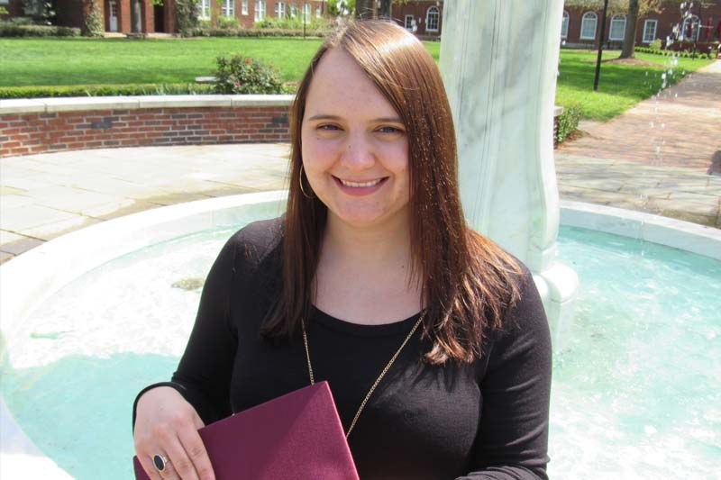 Profile photo of Rachael Martin standing on campus with her graduation cap in her hand