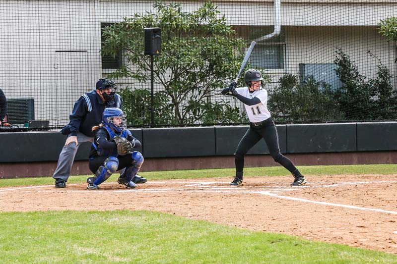 Meredith softball player up to bat with the catcher and umpire behind home plate