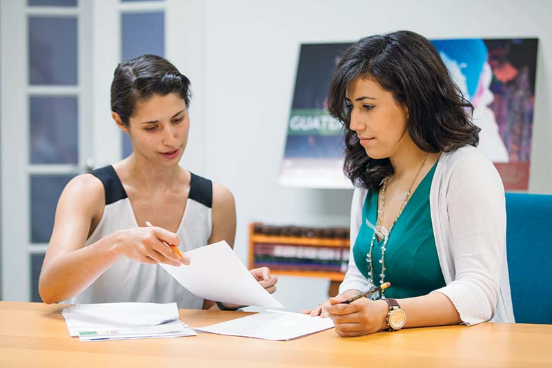 Two women looking at paperwork at a desk.