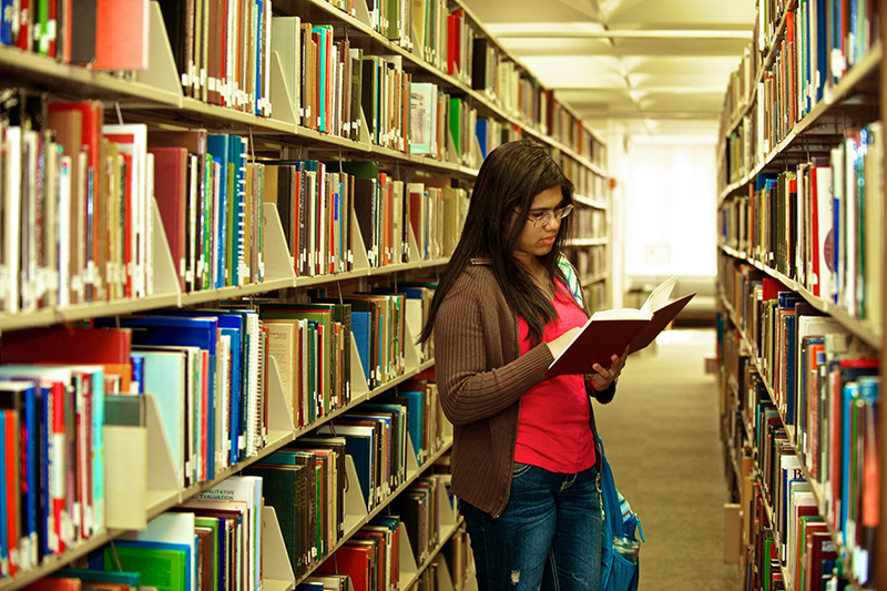 Student reading a book in library stacks