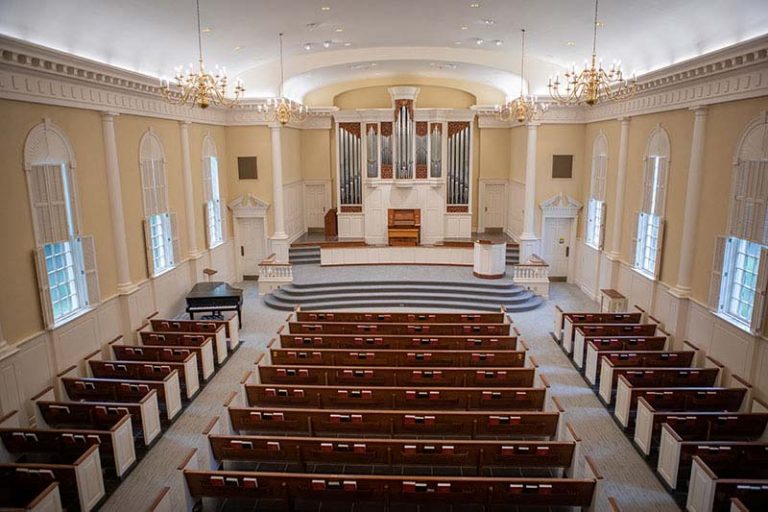 Image of the inside of the Meredith Chapel. Shows tan walls with multiple rows of pews and stairs leading to the alter and a large organ behind that.