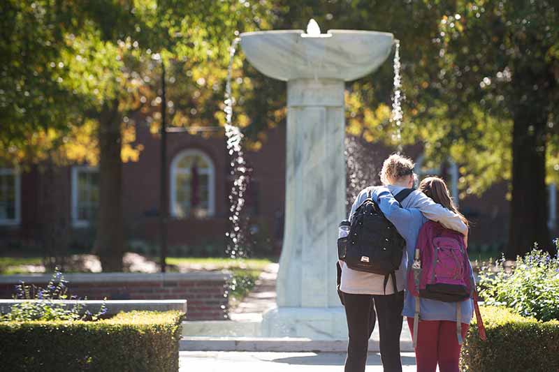 Two students with arms around each other at fountain in courtyard