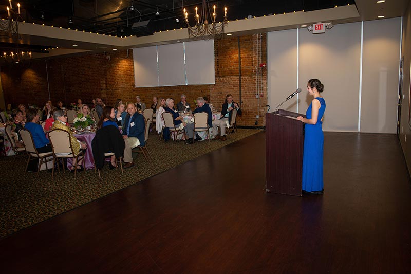 A woman giving a speech in front of guests at the scholarship dinner.