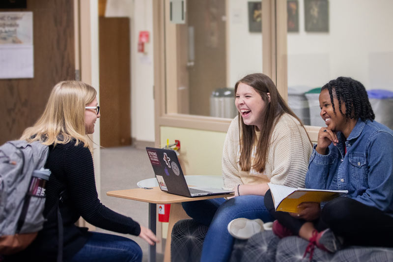 Three students talking and laughing in library learning center.