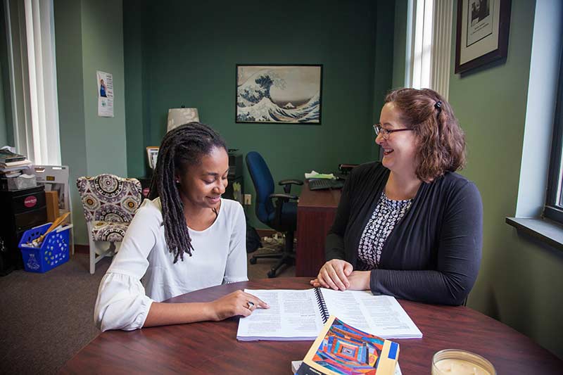 Joy Learman and Dielle McMillian talk at a desk over a social work booklet.