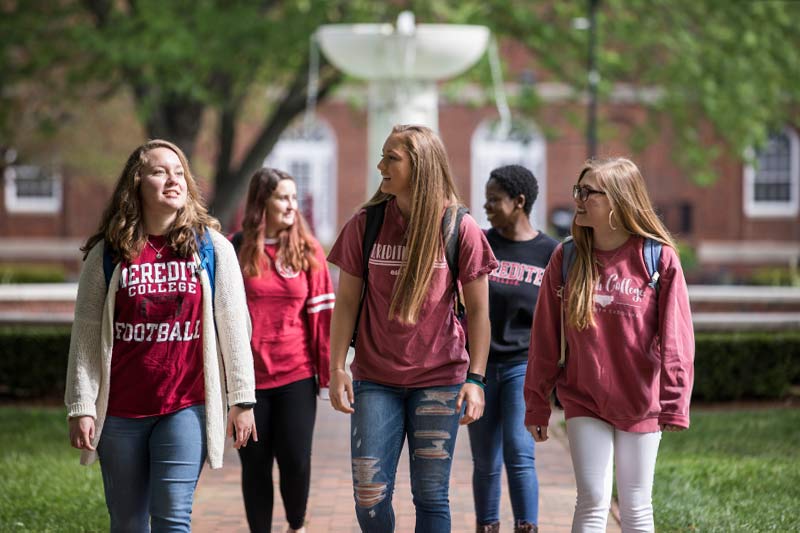 Five Meredith students walking on campus near fountain.