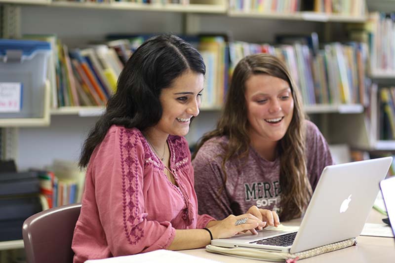 Two girls work on a computer and are laughing.