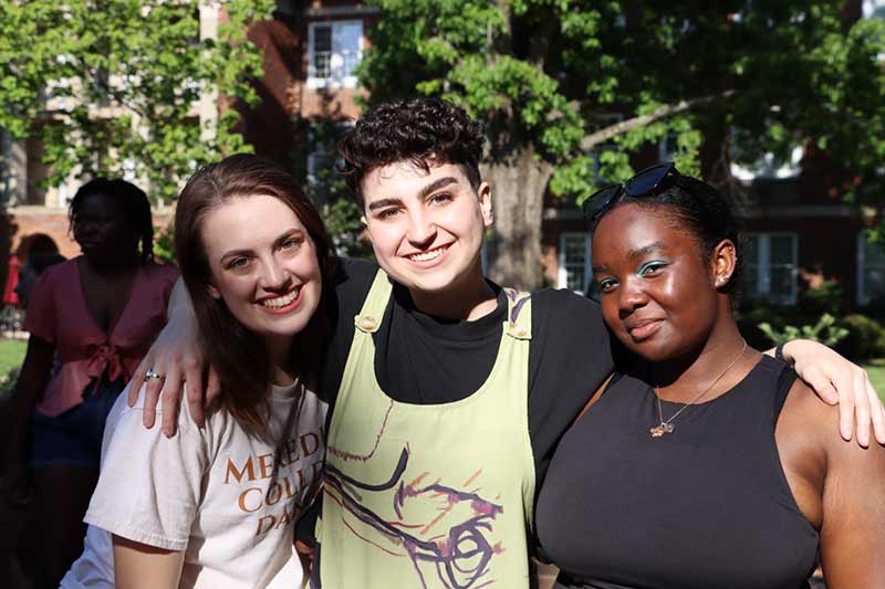 Three students smile in the courtyard.