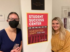 Two people stand next to a sign depicting where the Student Success Center is.