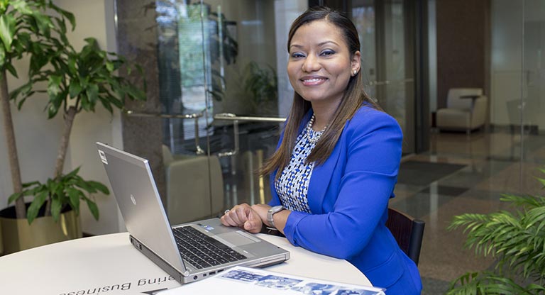 An MBA student in a bright blue jacket works at a laptop.