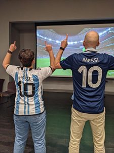 Two people wearing Messi jerseys watch the World Cup.