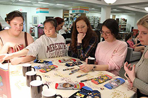Students in a group look at the prize table with mugs, socks, and pens.