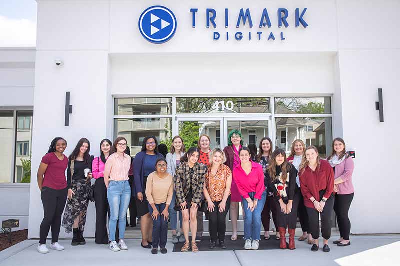 Students smiling in front of the Trimark Digital building.