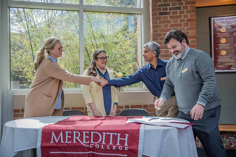 Four people shaking hands at the articulation agreement signing for our pre-health program with West Virginia University medical school.