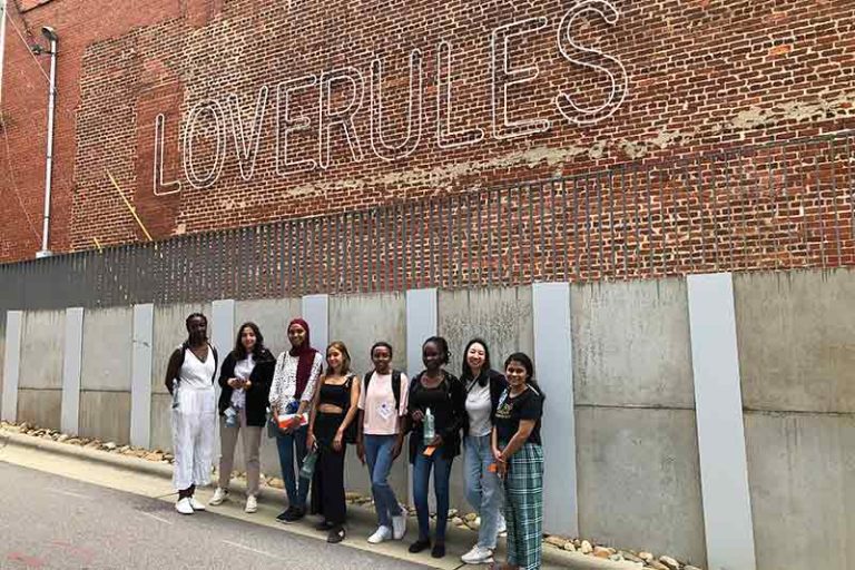Students beneath a brick wall with a glowing sign that says Love Rules.