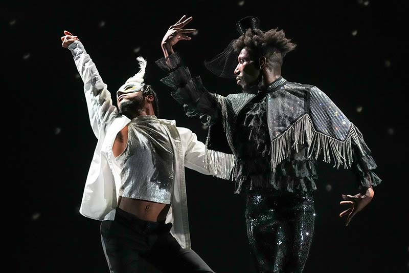 Two black dancers, one in black clothes and one in white, dancing.