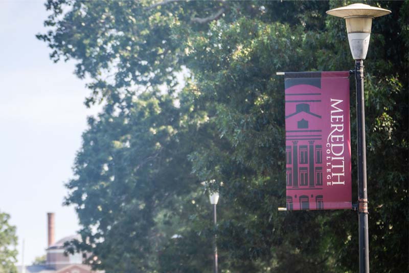 A meredith college banner on a lightpost on the main campus drive.