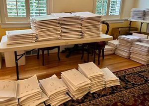 A table and room filled with stacks of back-to-school packets ready to be sent out.