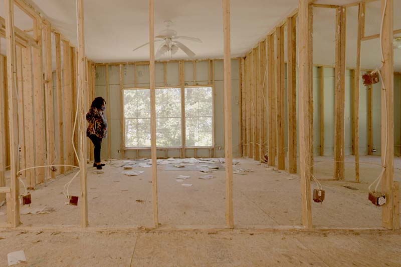 Woman stands in the frame of a water damaged house.