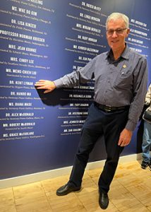 Kent Lyman pointing to his name on the wall for the Steinway and Sons Music Teacher Hall of Fame inductees.