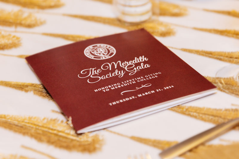 A program sitting on a gold and white tablecloth for the society gala.