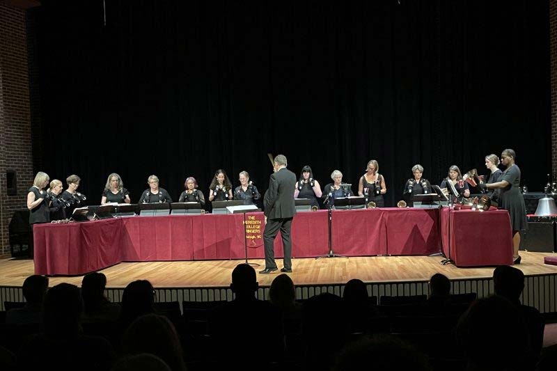 Ringers Choir group in Jones Auditorium playing handbells on stage with live audience.