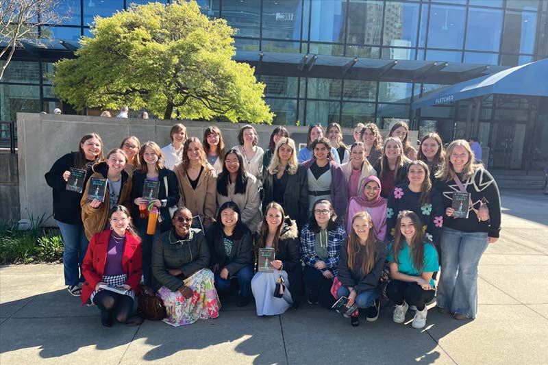 Honors Program Students posing together on a Group Trip in front of glass building.