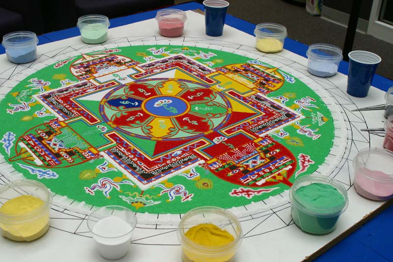 Tibetan Sand Mandala showing on table with cups of colored sand and working tools.